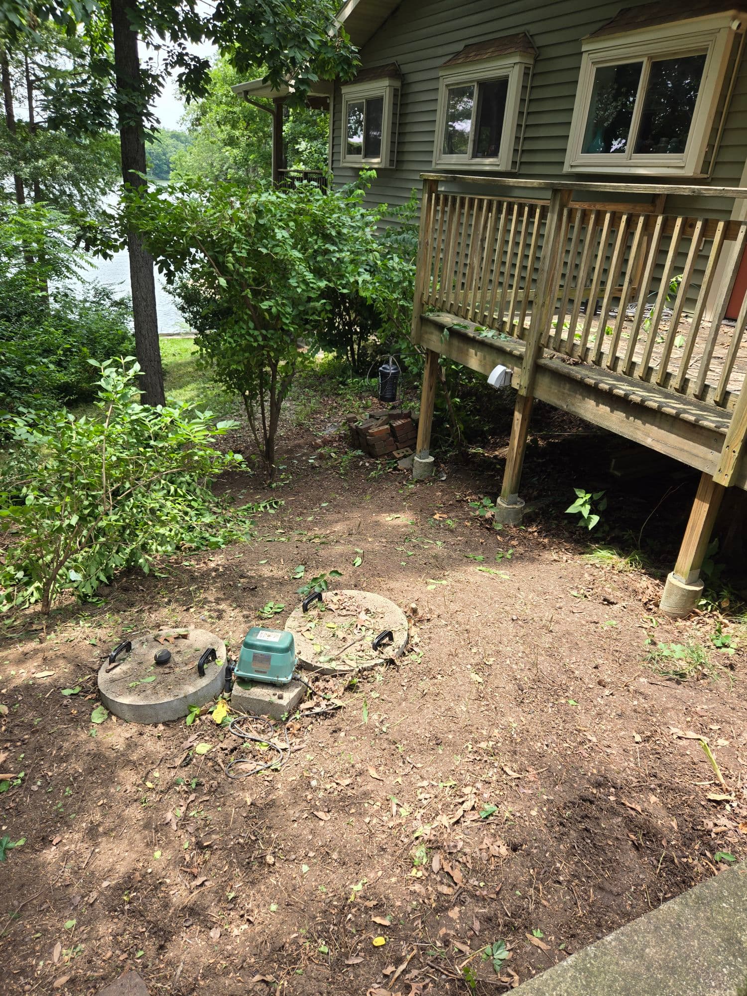 Backyard cleanup with cleared ground area, shrubs, and deck near a lakeside home — Jarjus Lawn Care